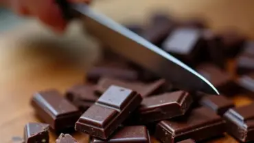 Hand chopping a vegan dark chocolate bar on a wooden cutting board