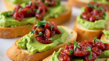 Creamy avocado and sun-dried tomato crostini on a platter.