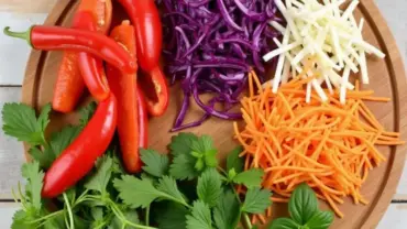 Colorful vegetables and fresh herbs arranged on a cutting board for vegan spring rolls.