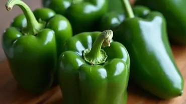 Four whole poblano peppers on a wooden cutting board