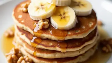 Stack of vegan banana oat pancakes on a plate with syrup and bananas.