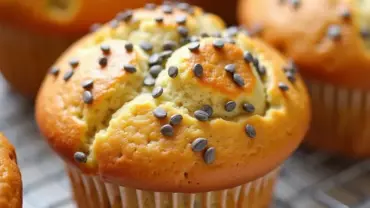 A batch of freshly baked vegan lemon poppy seed muffins cooling on a wire rack.