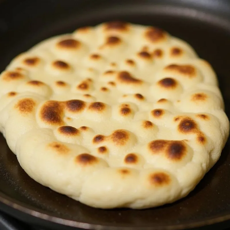 Vegan naan cooking on a cast-iron skillet